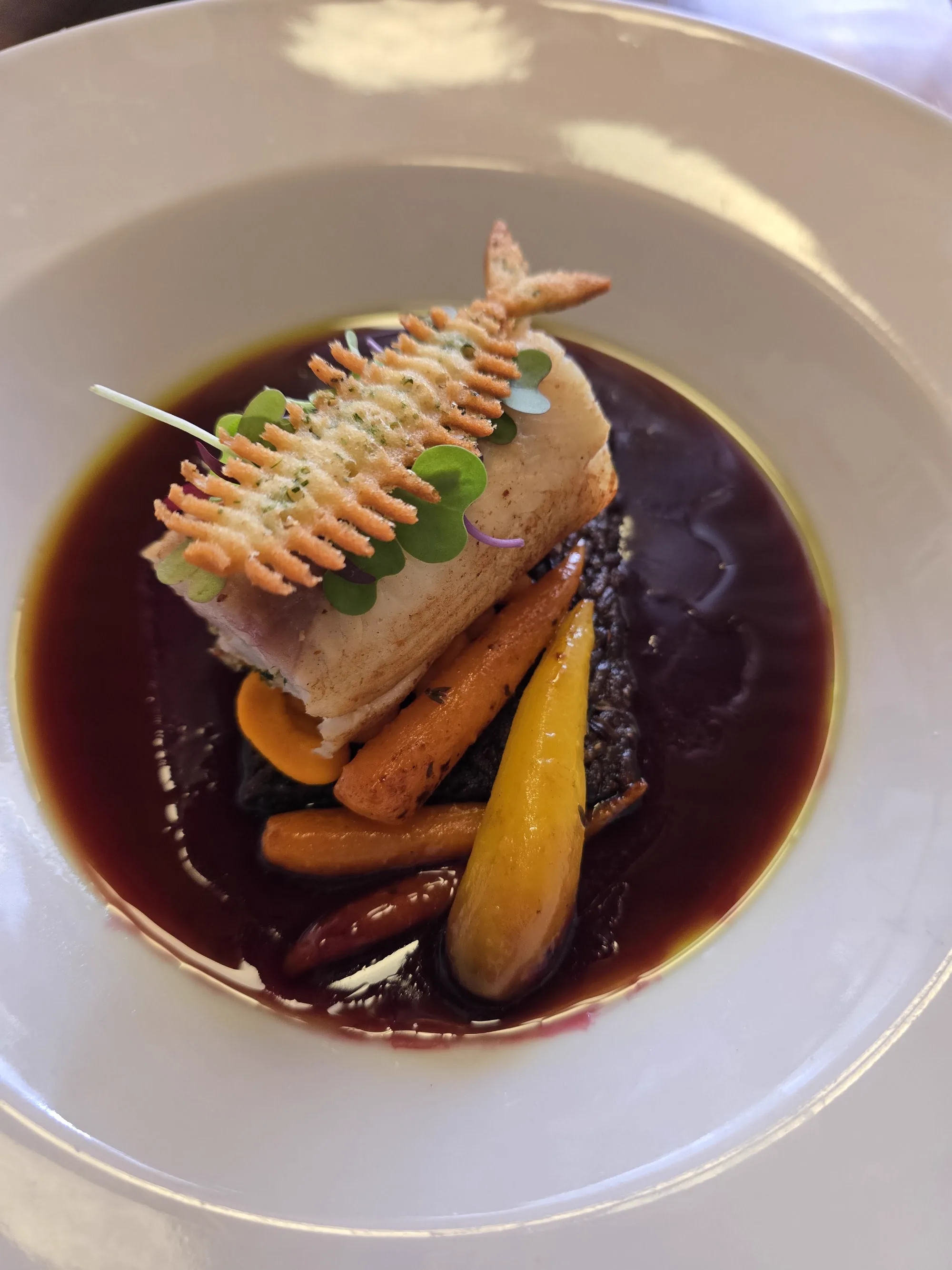 Pescado con una teja crocante en forma de espina sobre reducción de vino